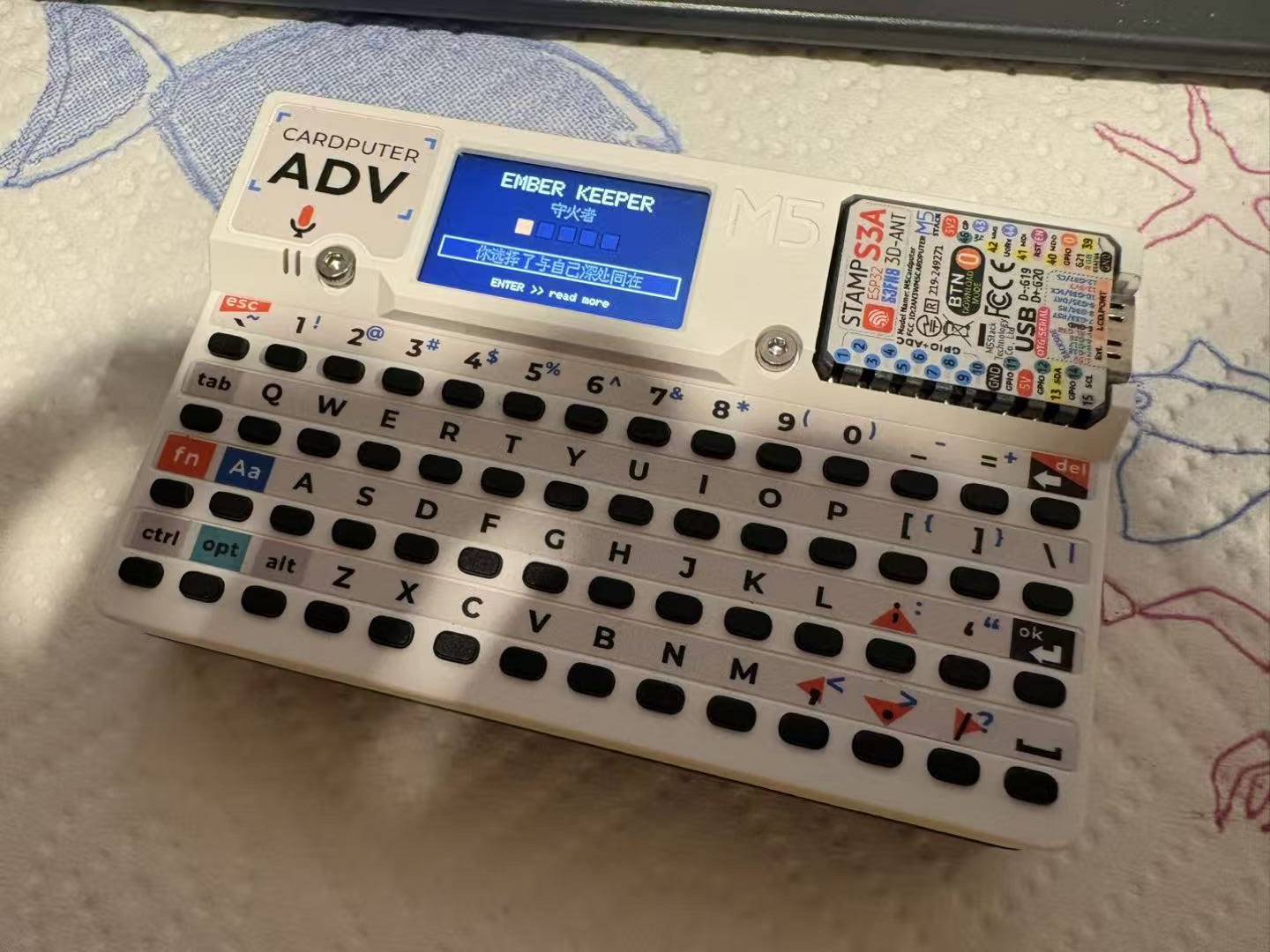 M5 Cardputer 显示 AI 生成的 reading——EMBER KEEPER / 守火者,五格光谱色块,中文短诗